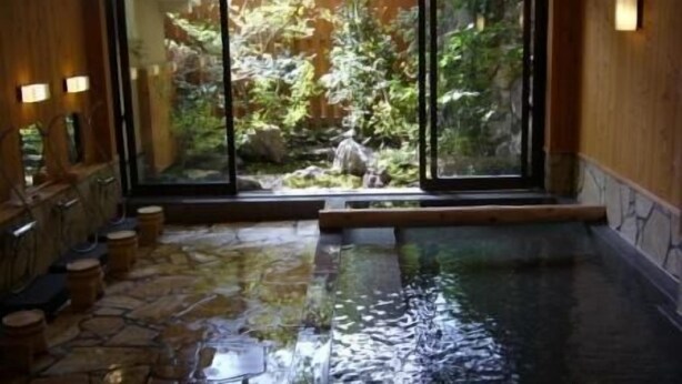 A stone-floored indoor pool with a view of a rocky garden through large windows. - Kurokawa Onsen Wafu Ryokan Misato (Minamioguni)