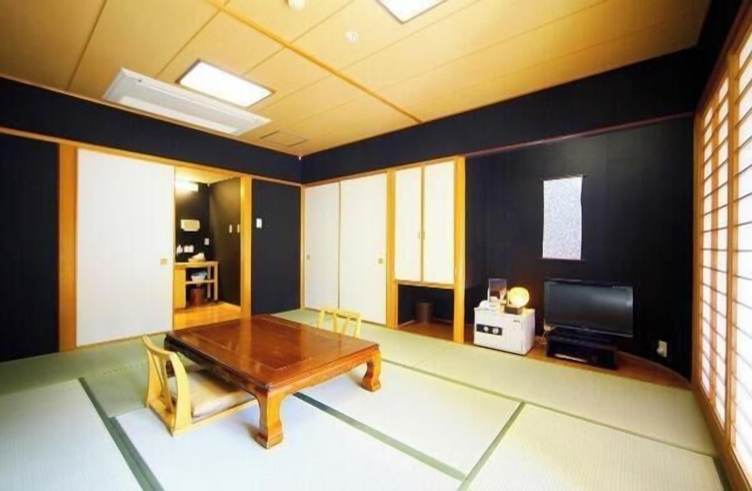 Ein traditioneller japanischer Raum mit Tatami-Böden, einem Holztisch, einem Fernseher und gleitenden Türen.