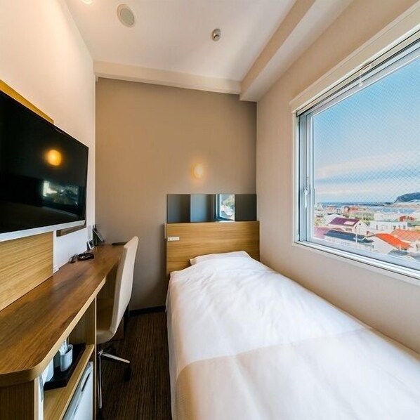 A hotel room with a bed, a desk with a computer, a TV, and a window with a city view. - Sekishuu no Yu Super Hotel Gotsu Ekimae (Gotsu)