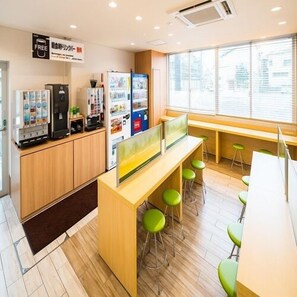 Un café moderno con mostrador de madera, taburetes verdes y máquinas expendedoras.