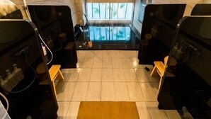 A spa room with two black massage chairs, a small wooden stool, and a large window with a view of palm trees. - Sekishuu no Yu Super Hotel Gotsu Ekimae (Gotsu)