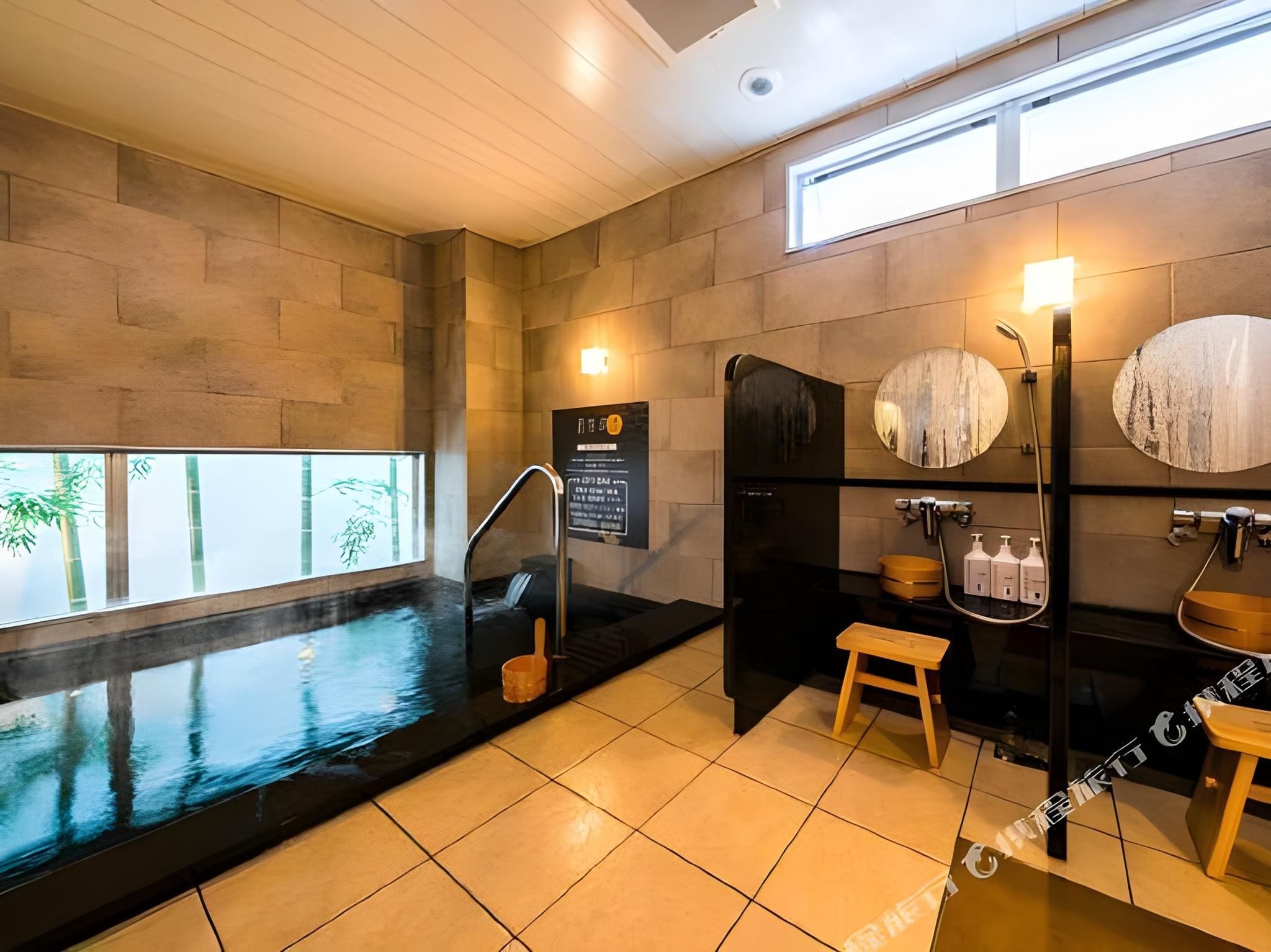 Un spa moderno con una amplia bañera negra, un taburete de madera y un espejo instalado en la pared.
