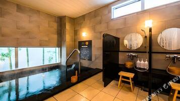 Un spa moderno con una amplia bañera negra, un taburete de madera y un espejo instalado en la pared.