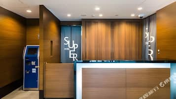 A hotel reception area with a wooden reception desk, a blue information kiosk, and a large sign with the hotel's name.