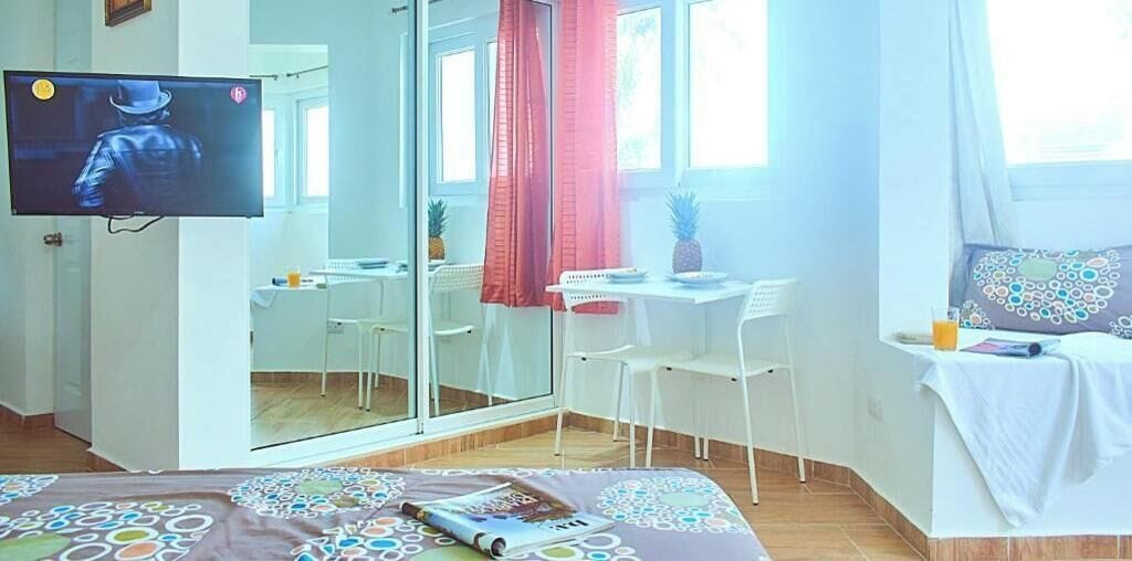 Una habitació amb un llit, una taula de treball, una cadira, un televisor i una finestra amb cortines.