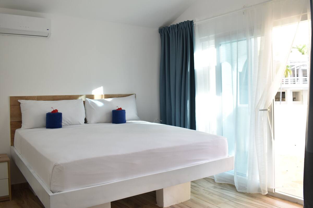 A large bed with white linens, a wooden headboard, and two blue pillows.