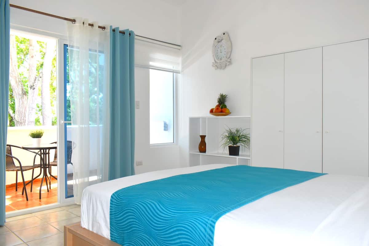 A bedroom with a bed, a window, a door, and a view of the outside.