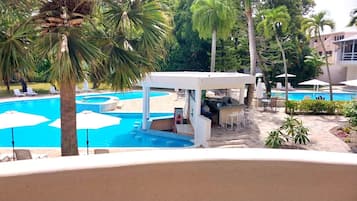 Relax by the pool surrounded by palm trees and lush greenery, with a bar area and waterfall nearby.