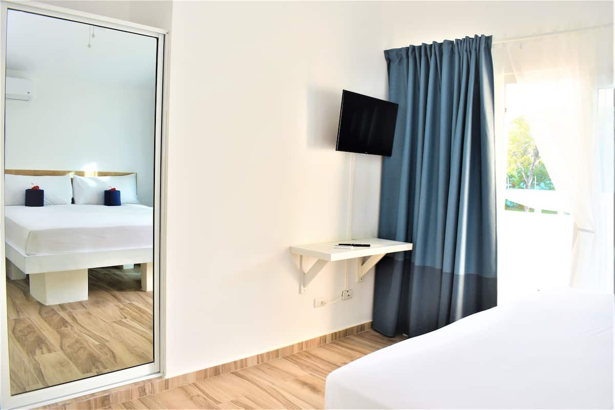 A hotel room with a bed, a TV mounted on the wall, a small bedside table, and a window with curtains.