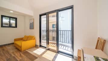 Una habitación con un sofá amarillo, una mesa de madera y un ventanal corredero que da a un balcón.