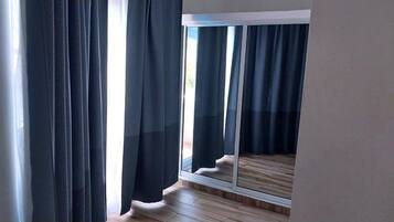 A room with a large window, wooden flooring, and dark curtains.