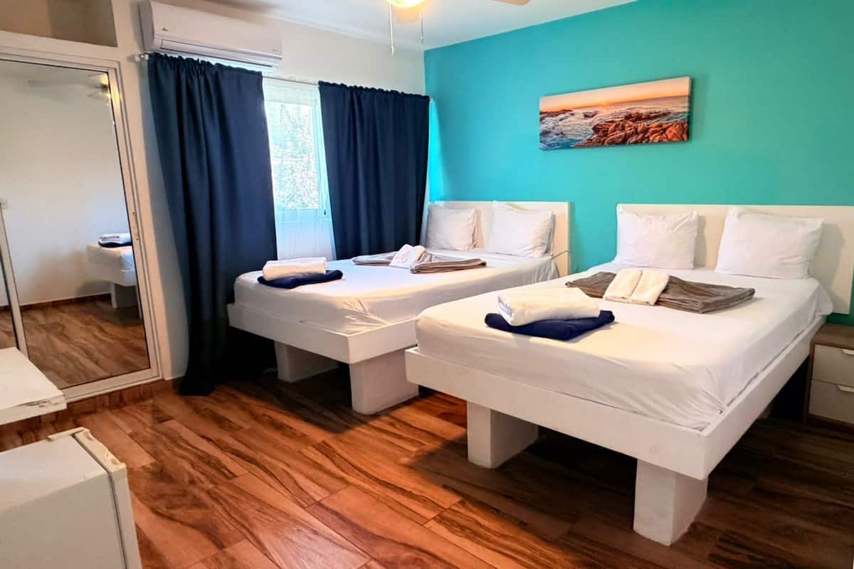 A room with two beds, a mirror, a window with curtains, and a painting on the wall.