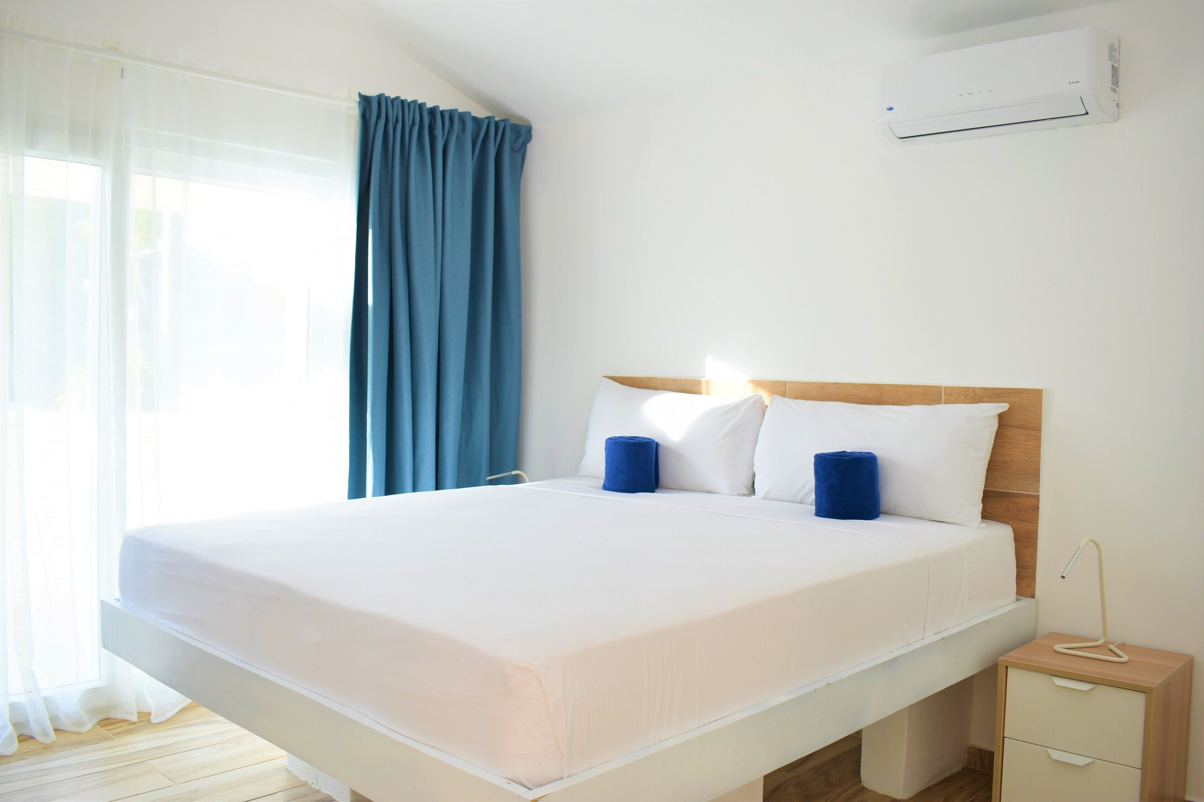 A neatly made bed with white linens, a wooden headboard, and two blue pillows.