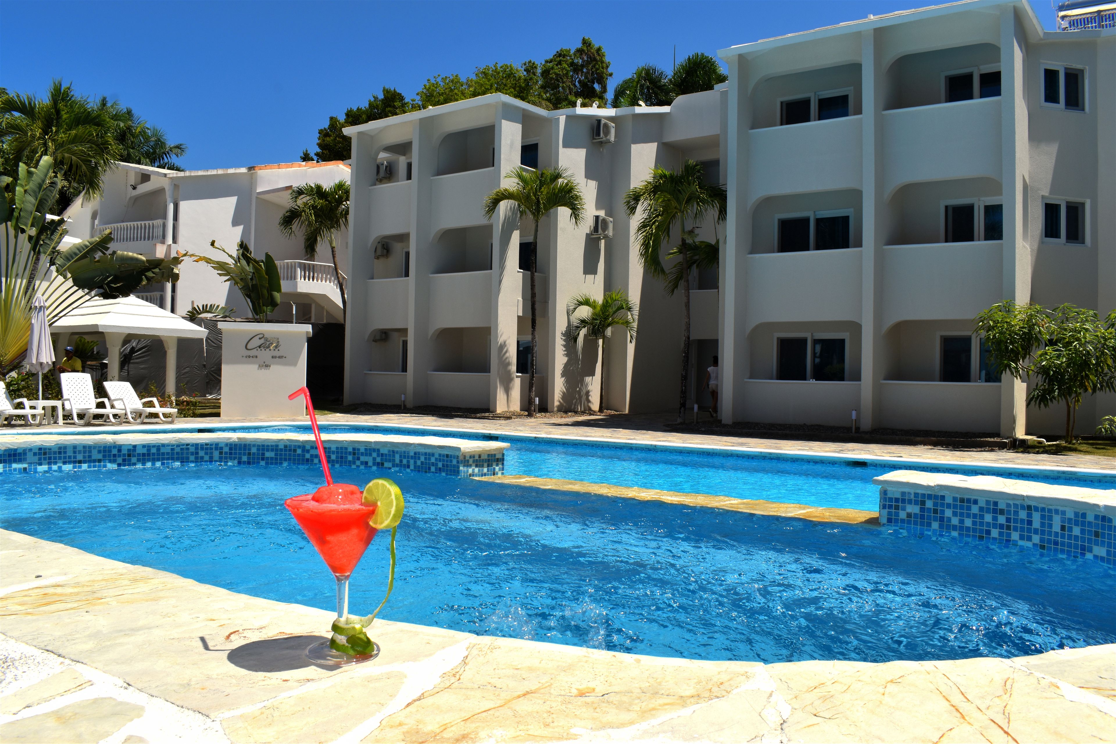Una piscina con un drink sul bordo, circondata da un edificio con balconi e palme.