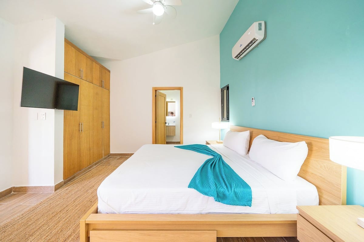 A hotel room with a bed, wooden wardrobe, TV, air conditioning unit, and a bathroom visible through an open door.