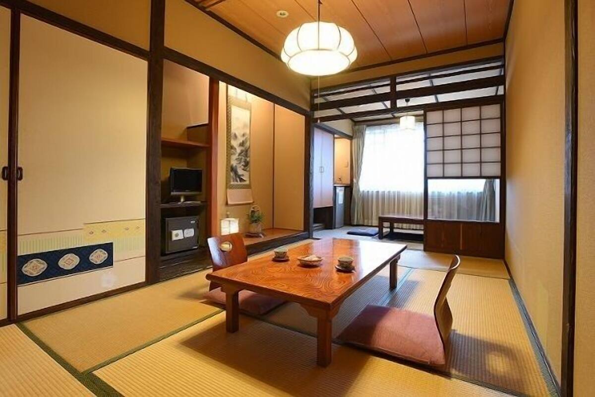 Une pièce de style japonais traditionnel, avec un sol recouvert de tatamis, une table en bois, des portes coulissantes et un luminaire suspendu.