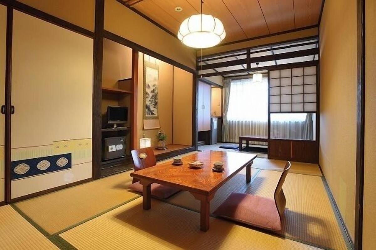 Une pièce traditionnelle japonaise avec un sol recouvert de tatamis, une table en bois, des portes coulissantes et une vue à travers un paravent shoji.