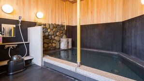 A hot spring bath with a stone wall, wooden paneling, and a stone bench. - Extol Inn Sanyo Onoda Asa Ekimae (Sanyoonoda)