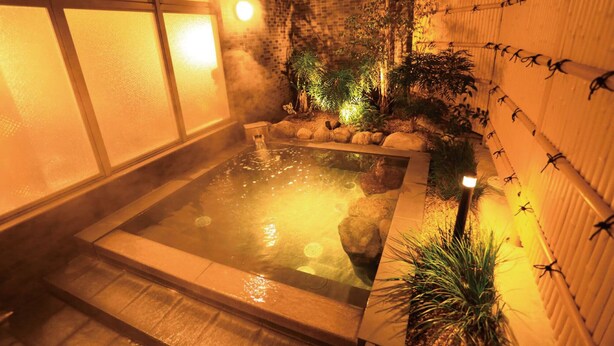 A hot spring area with a stone bath, surrounded by plants and a brick wall. - Extol Inn Sanyo Onoda Asa Ekimae (Sanyoonoda)