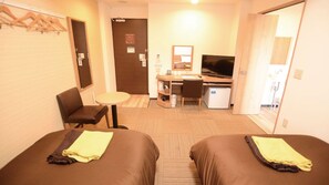 Hotellihuone, jossa on kaksi sänkyä, työpöytä, tuoli, televisio ja pieni jääkaappi.