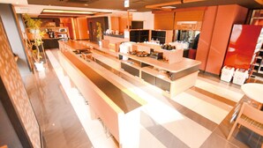 A modern hotel lobby with a long reception desk, seating area, and a large window providing a view of the interior. - Extol Inn Sanyo Onoda Asa Ekimae (Sanyoonoda)