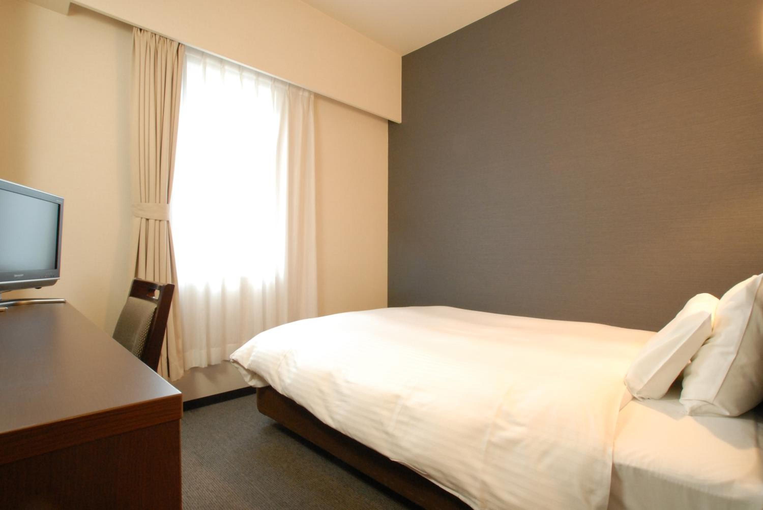 A hotel room with a bed, a desk, and a television.