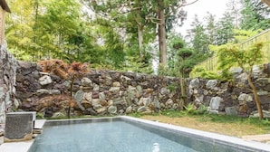 A rectangular swimming pool with a stone wall and trees in the background. - Hakone Suishoen (Hakone)
