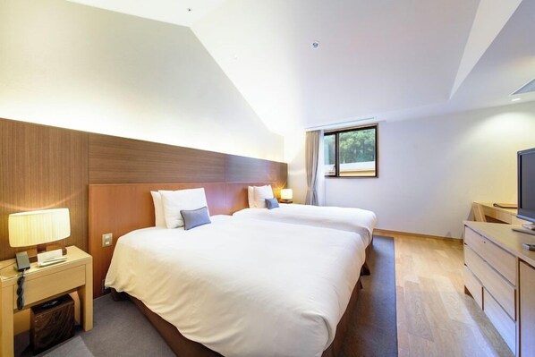 A hotel room with two beds, a desk with a lamp, a television, and a window with curtains. - Hakone Suishoen (Hakone)