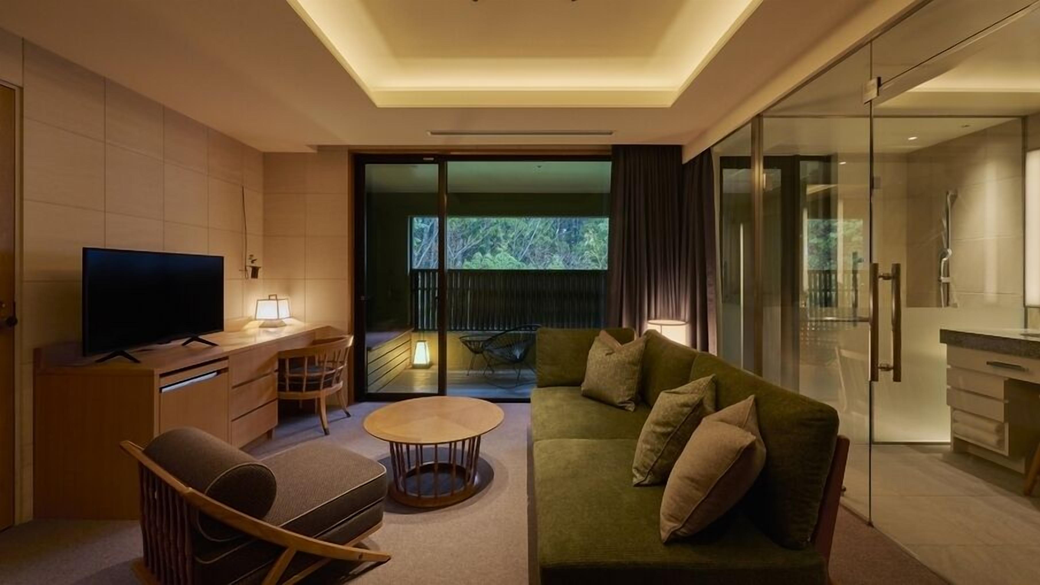 A modern living room with a flat-screen TV, a sofa, a coffee table, and a dining area with a glass partition.