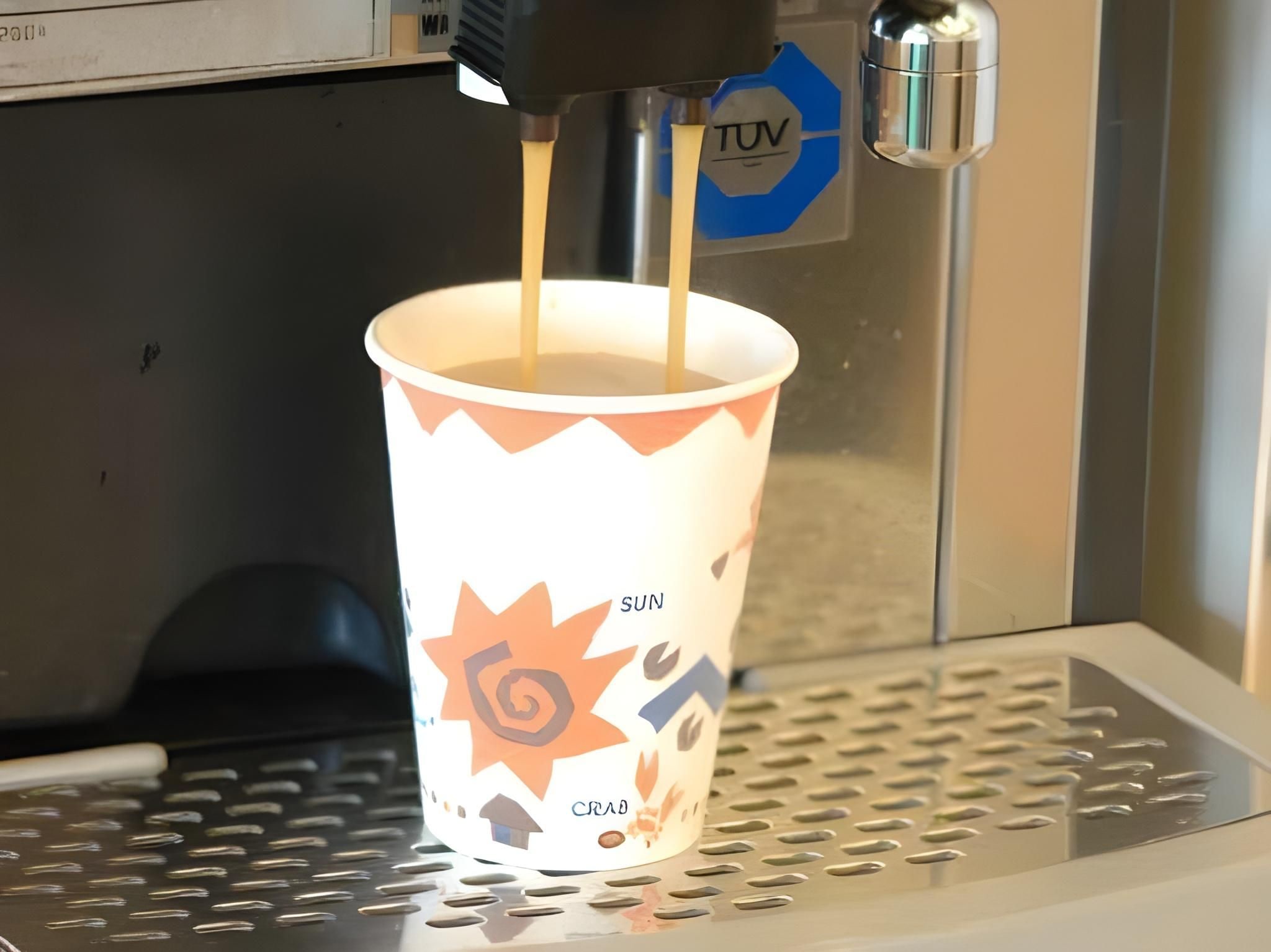Une tasse en papier ornée d’un motif représentant un soleil et un crabe, dans laquelle on verse une boisson provenant d’une machine distributrice.