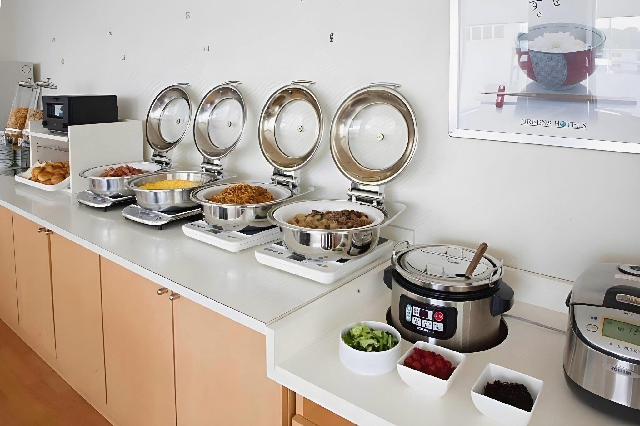 Disposição de buffet com diversos alimentos e um cozedor de arroz.