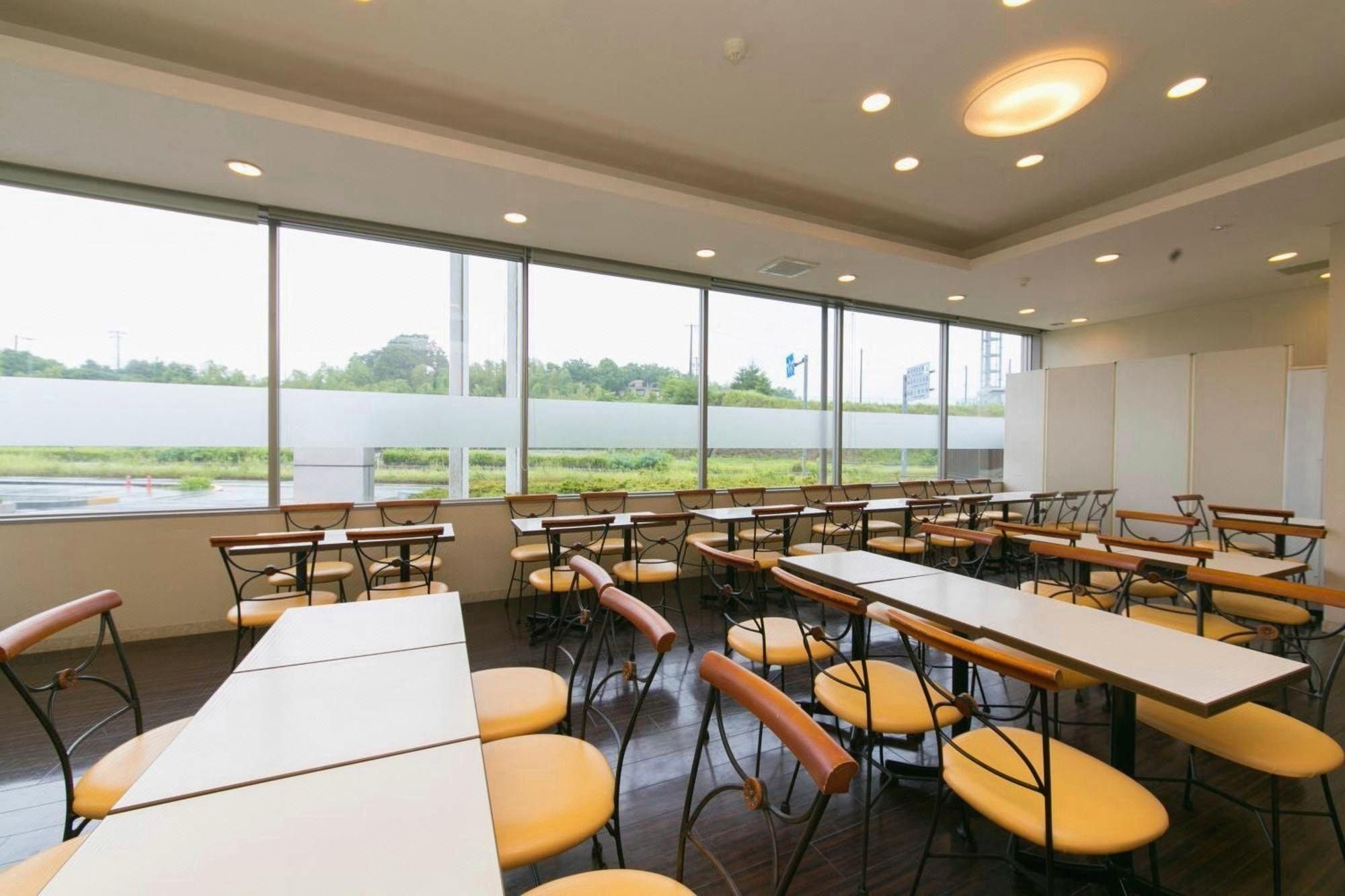 A classroom with tables and chairs, large windows, and a view of a field.