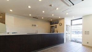 A hotel reception area with a counter, ceiling lights, a clock, and a door leading outside. - Hotel Econo Taki (Taki)