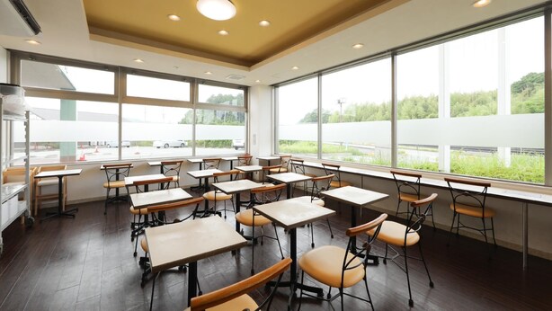 A classroom with desks and chairs arranged in rows, large windows with a view of greenery and a road, and a ceiling with recessed lighting. - Hotel Econo Taki (Taki)