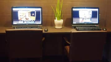 Two laptops on a wooden desk with a potted plant between them.