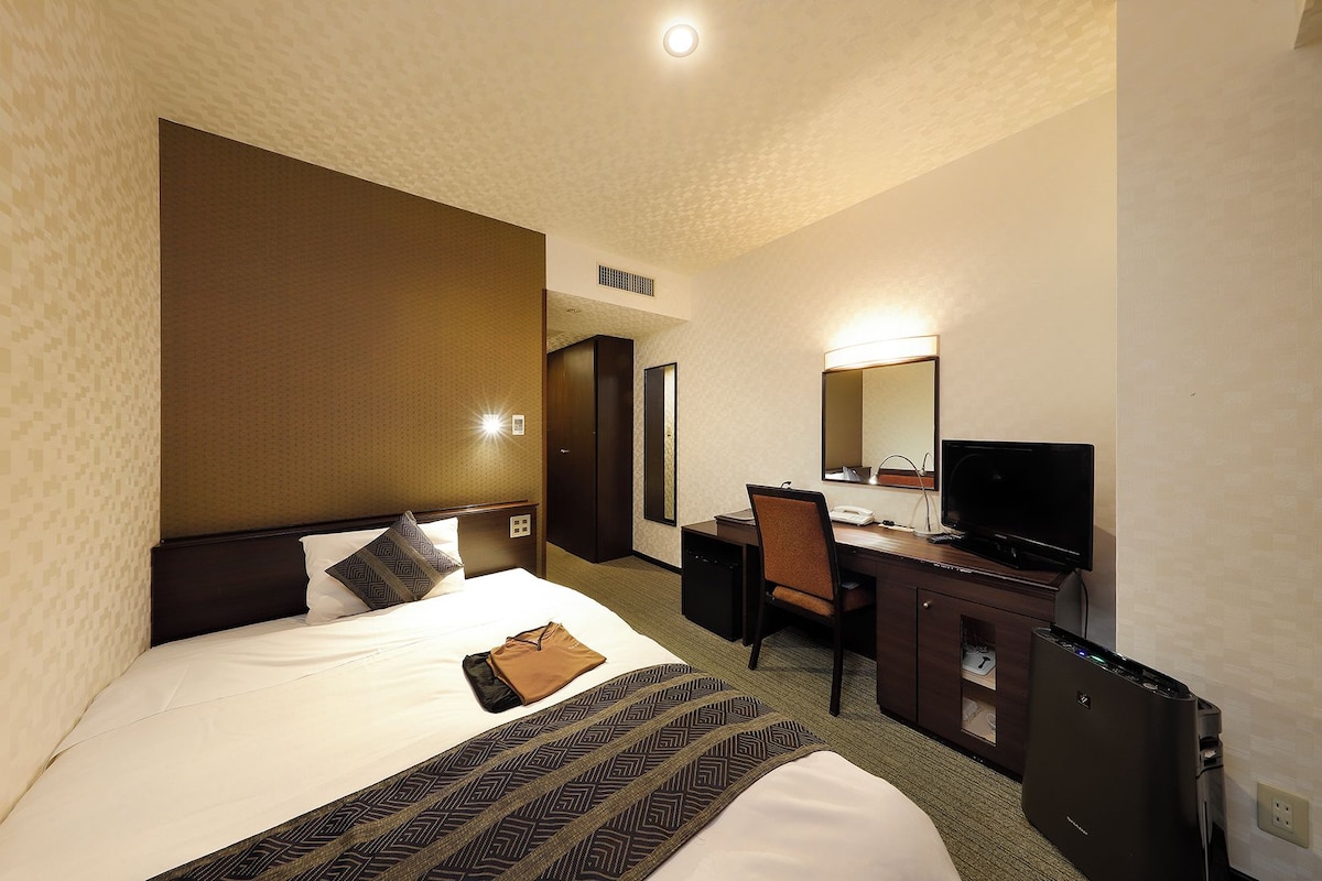 A hotel room with a bed, a desk, a television, and a wardrobe.