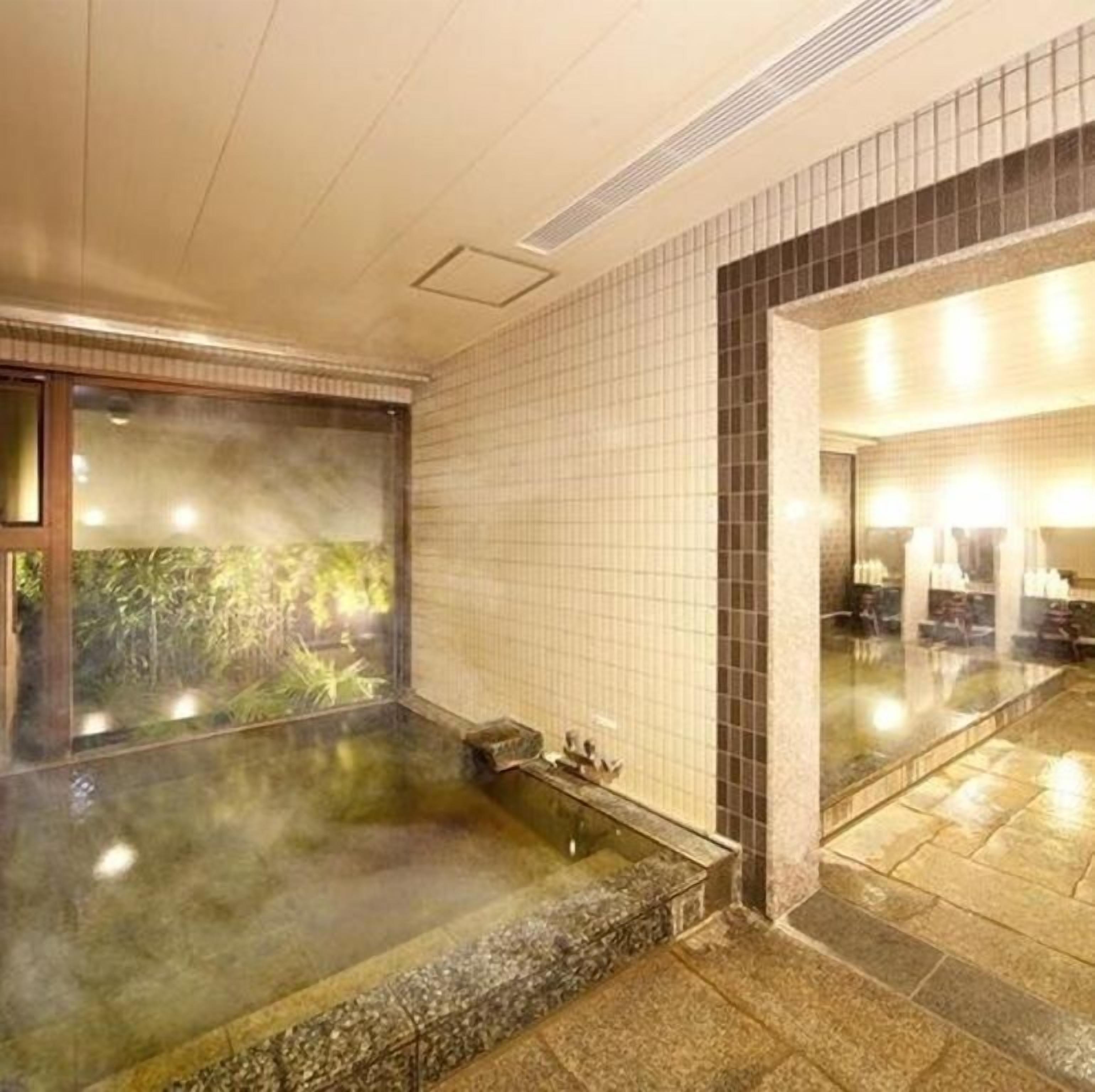 A spa area with a hot tub, tiled walls, and a view of greenery outside.