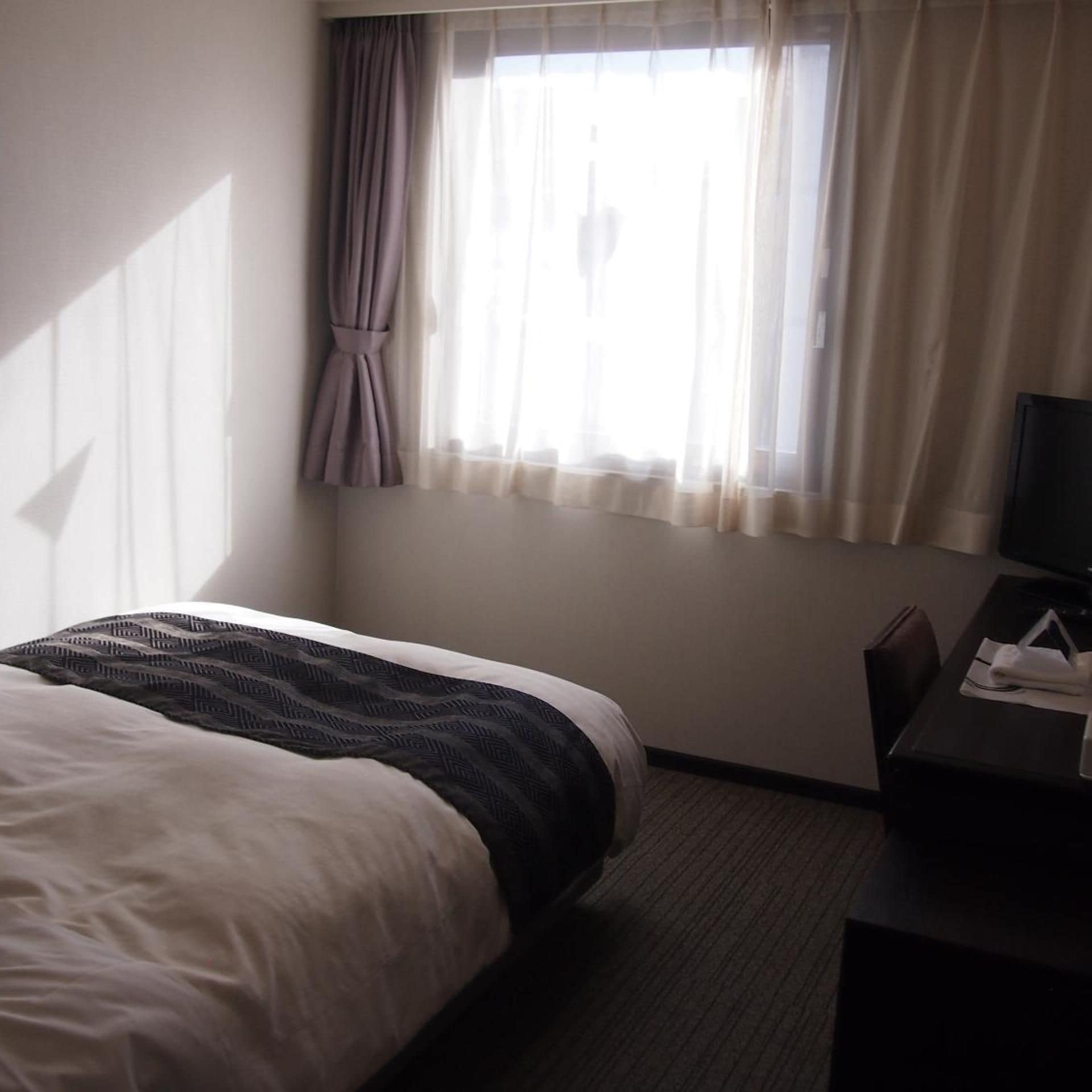 A hotel room with a bed, a desk, and a window with curtains.