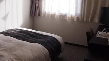 A hotel room with a bed, a desk, and a window with curtains.