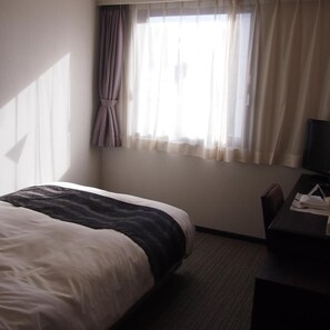Een hotelkamer met een bed, een bureau en een raam met gordijnen.
