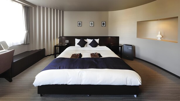 Hotelkamer met een groot bed, een bureau, een stoel, een nachtkastje, een lamp en een wandplank.