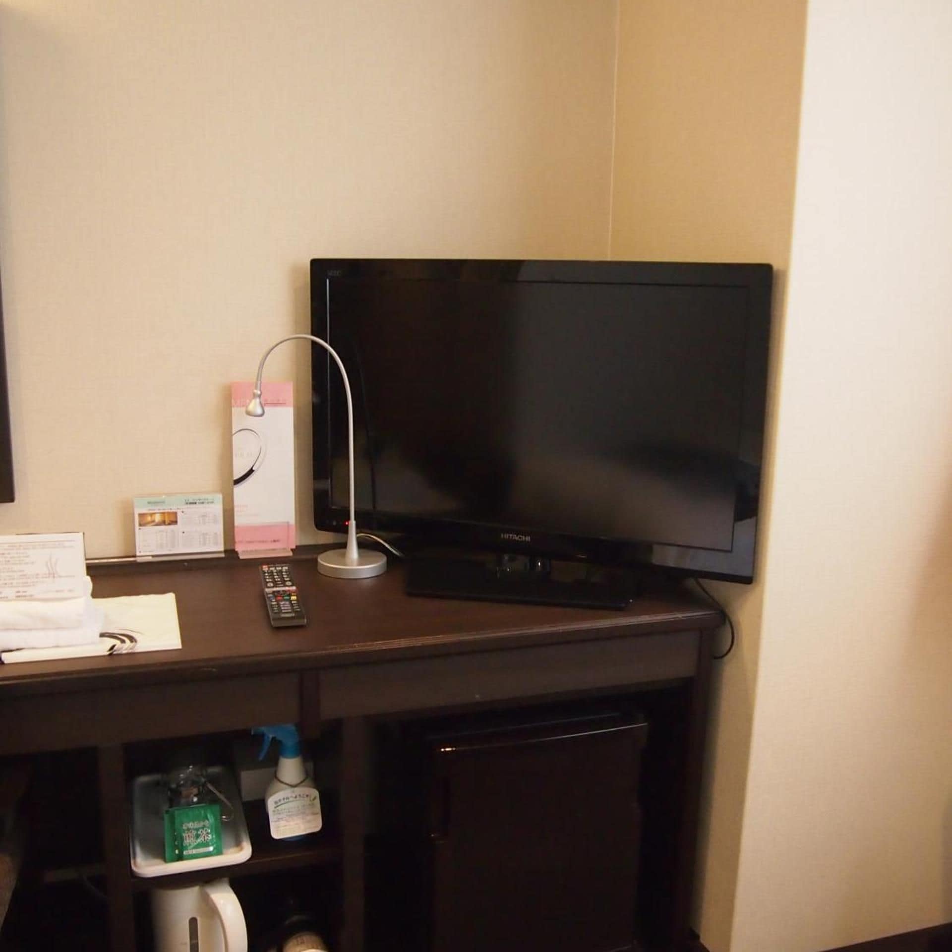 A hotel room with a flat-screen TV mounted on the wall, a remote control, and a small shelf with toiletries.