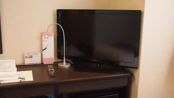 A hotel room with a flat-screen TV mounted on the wall, a remote control, and a small shelf with toiletries.