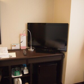 Een hotelkamer met een flatscreen televisie aan de muur, een afstandsbediening en een klein plankje met toiletartikelen.