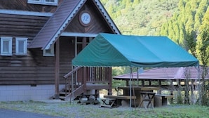 Uma cabana de madeira com varanda, um dossel verde e uma mesa de piquenique.