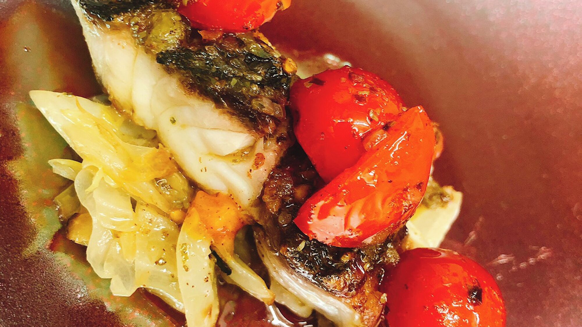 A close-up of a dish with fish, tomatoes, and cabbage.