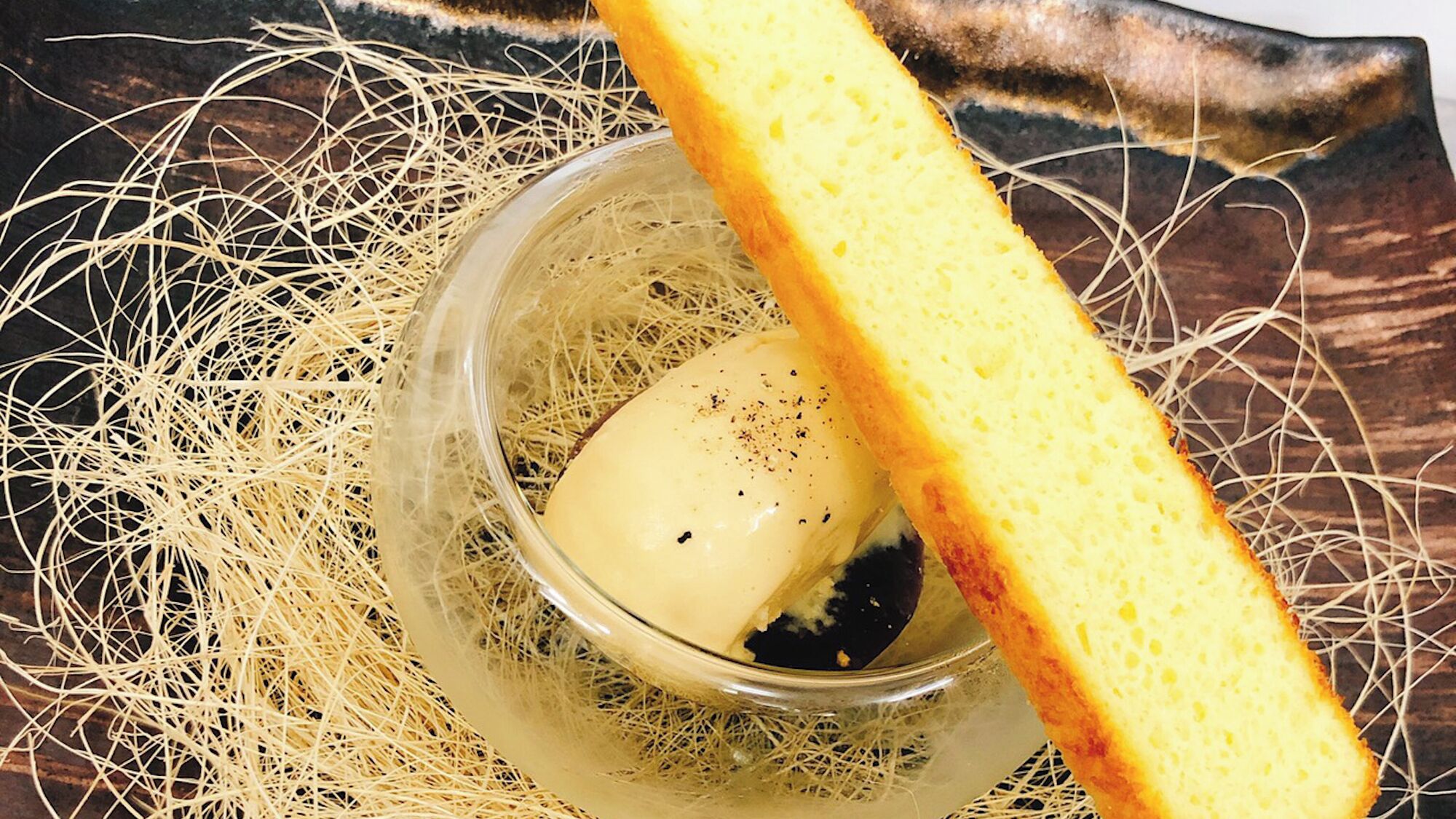 A glass bowl containing a piece of butter with a slice of bread on a textured surface.