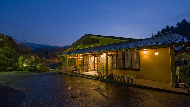 Une maison traditionnelle japonaise, avec un toit recouvert de tuiles, une véranda en bois et des plantes en pot.