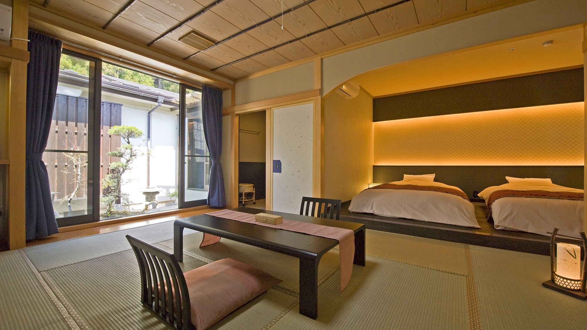 Ein traditioneller japanischer Raum mit Tatami-Boden, einem niedrigen Tisch, einer Couch und einem Bett mit Kopfteil.
