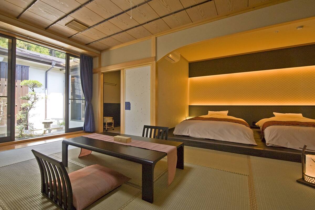 Une pièce de style japonais traditionnel, avec un sol recouvert de tatamis, une table basse, un canapé et un lit doté d’une tête de lit.